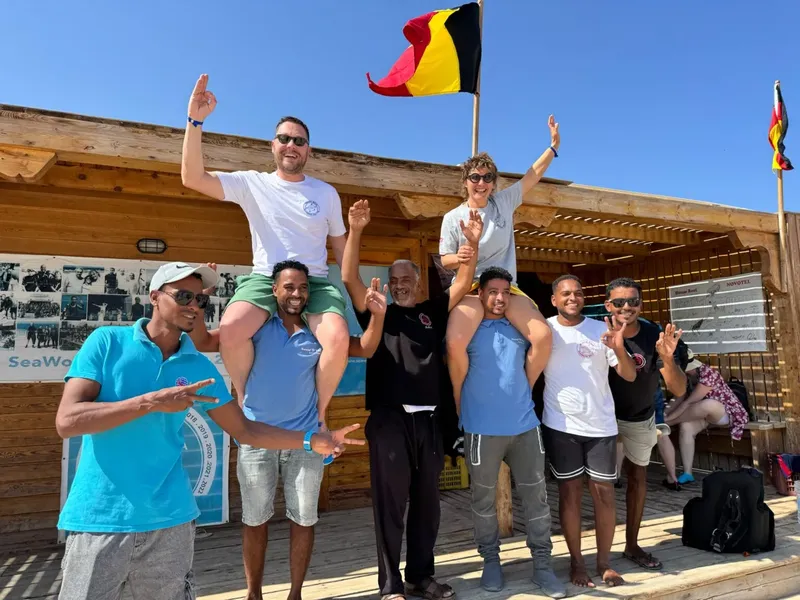 Groupe de personnes souriantes saluant devant une structure en bois