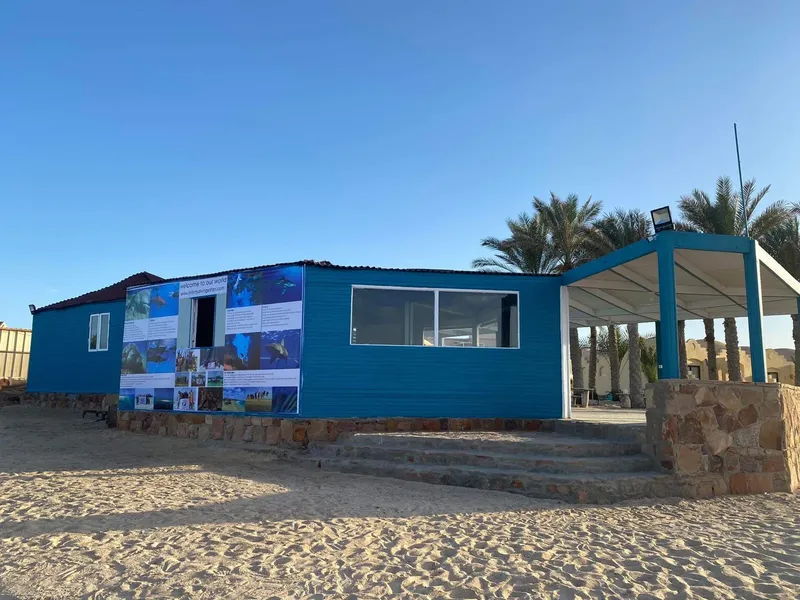 Bâtiment bleu avec des affiches de plongée, plage de sable et ciel clair
