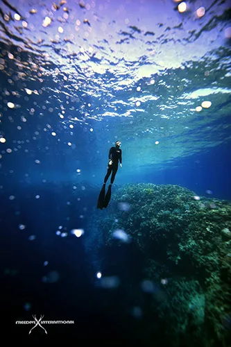Apnéiste en plongée libre, nageant vers la surface dans l'eau bleue