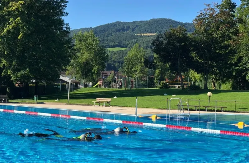 Plongeurs s'entraînent dans une piscine extérieure ensoleillée avec montagne