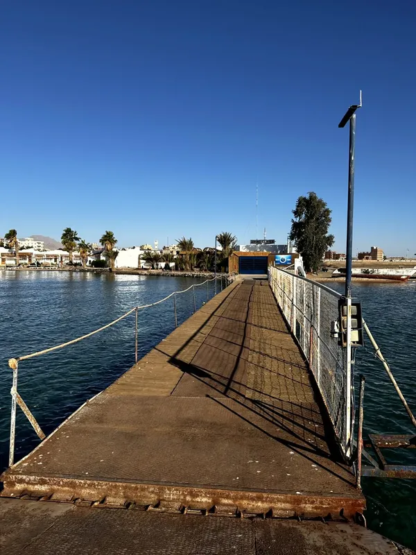 Ponton en bois s'étendant vers la mer sous un ciel bleu clair