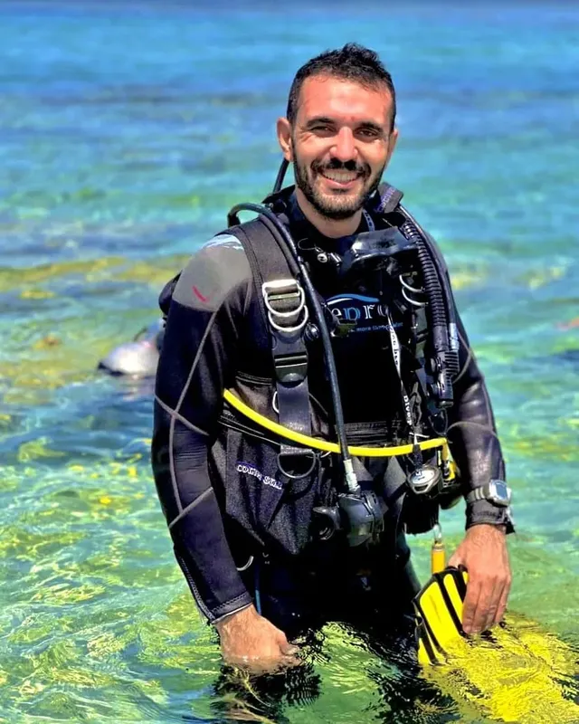 Plongeur souriant en combinaison, équipé, dans une eau turquoise claire