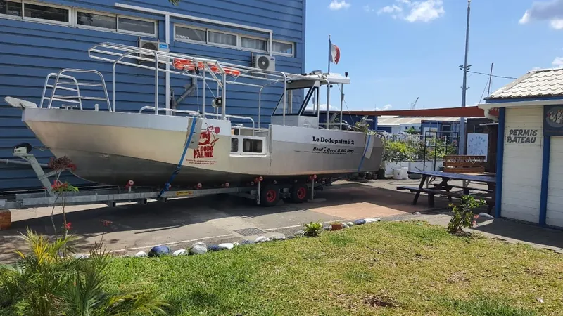 Bateau de plongée argenté sur remorque devant un bâtiment bleu et un panneau