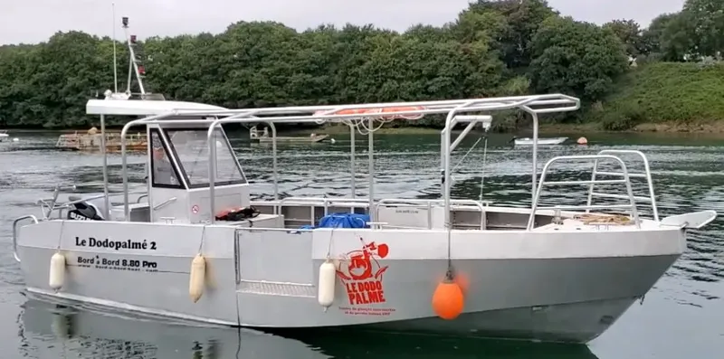 Bateau de plongée gris amarré sur l'eau calme avec logo visible