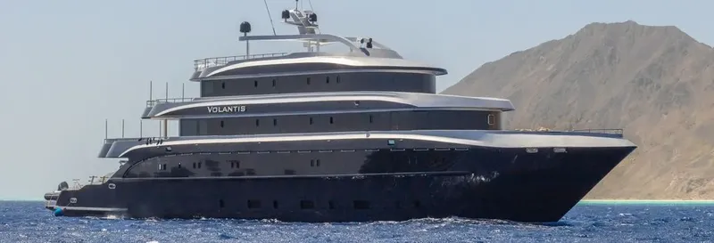 Grand yacht noir en mer avec des montagnes en arrière-plan