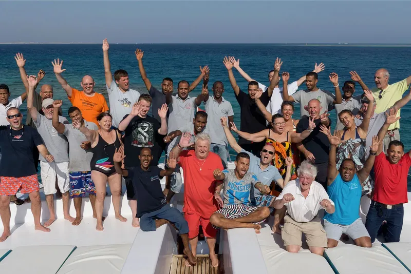 Groupe de personnes souriantes et levant les bras sur un bateau