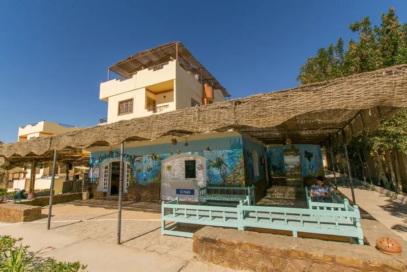 Façade d'un centre de plongée avec des structures ombragées et des personnes