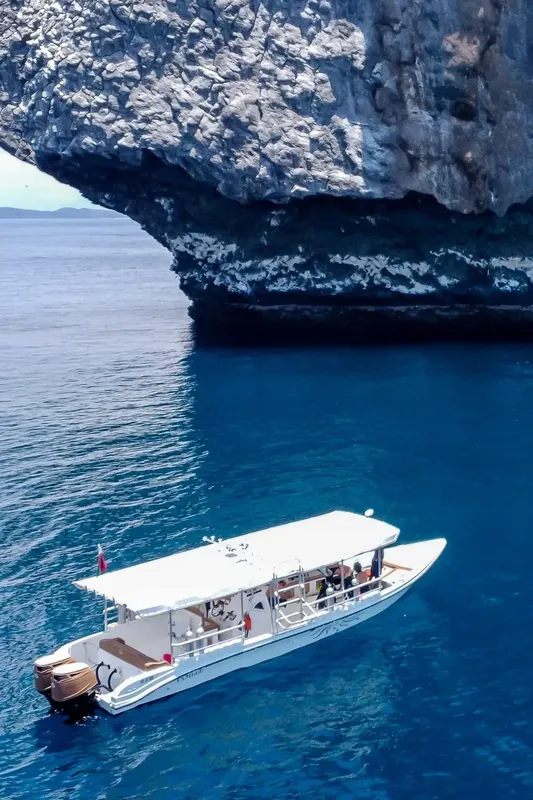 Bateau de plongée blanc navigue sous une falaise rocheuse en mer bleue