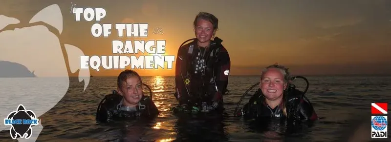 Trois plongeurs souriants en combinaison, équipés, dans l'eau au coucher du soleil