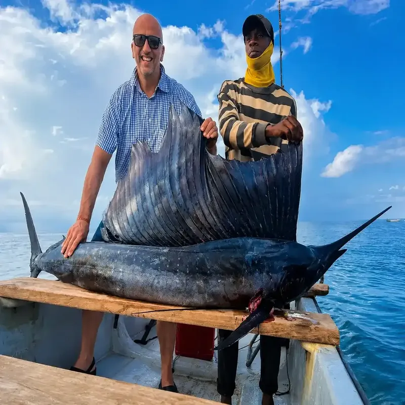 Deux hommes sourient, tenant un grand marlin bleu sur un bateau