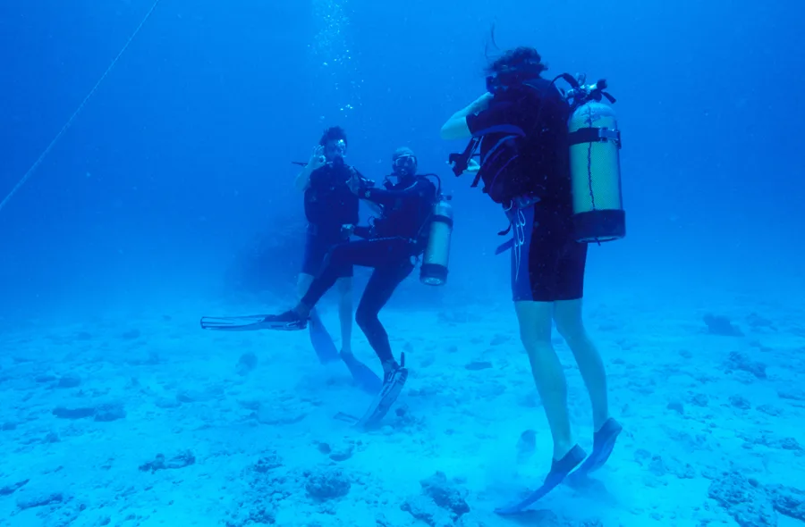 Trois plongeurs en combinaison interagissent sous l'eau dans un environnement bleu