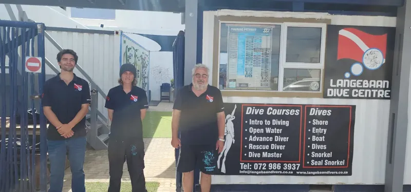 Trois personnes souriantes devant l'entrée d'un centre de plongée