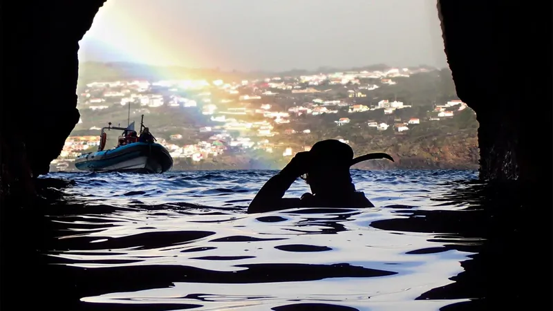 Plongeur en silhouette émerge d'une grotte face à un bateau et la côte