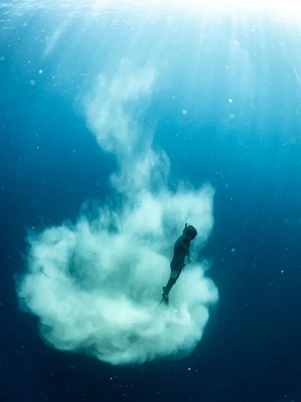 Apnéiste descendant dans une eau turquoise au milieu d'un nuage