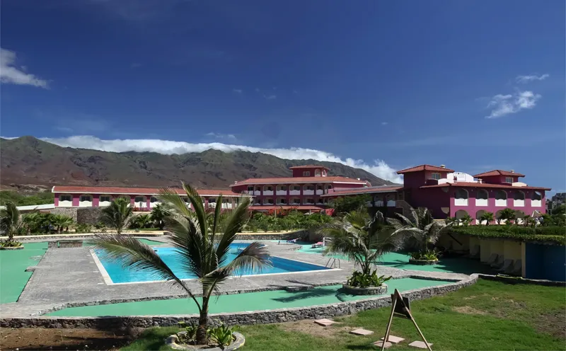Bâtiment rose avec piscine et végétation luxuriante sous ciel bleu