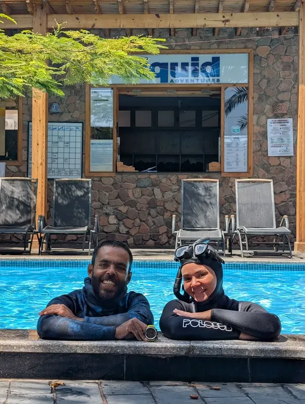 Deux plongeurs souriants au bord d'une piscine devant un centre