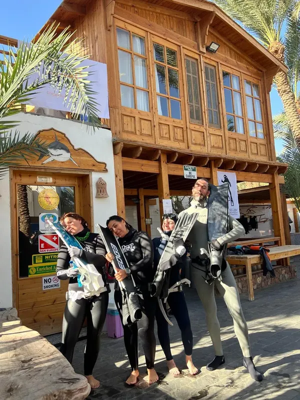 Quatre plongeurs en combinaison devant le bâtiment du centre de plongée