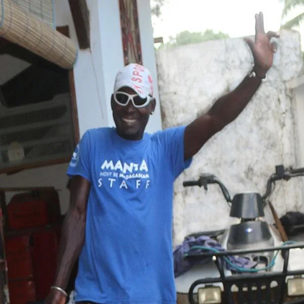 Homme souriant portant un t-shirt bleu avec un signe de la main