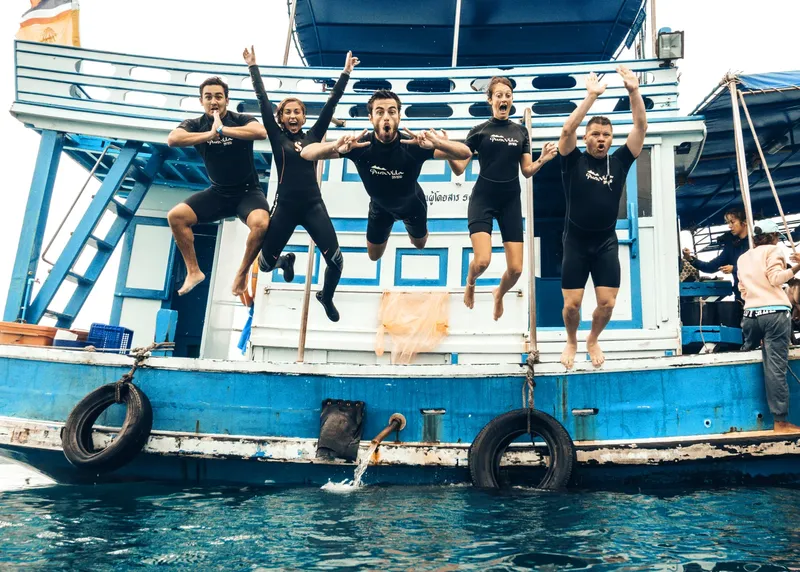 Groupe de plongeurs sautant d'un bateau bleu en mer
