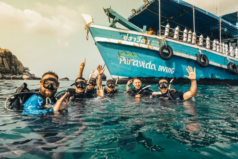 Plongeurs souriants et enthousiastes près d'un bateau bleu turquoise