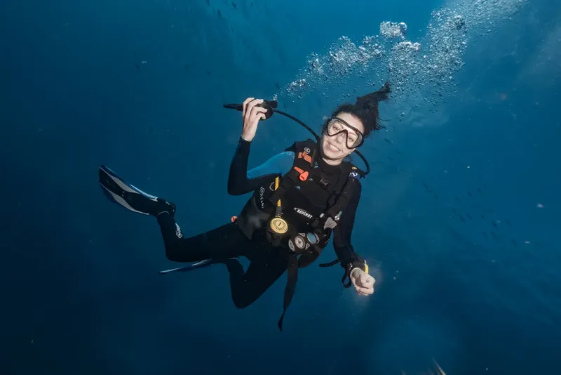 Plongeuse souriante en combinaison, donnant un signe de validation sous-marin