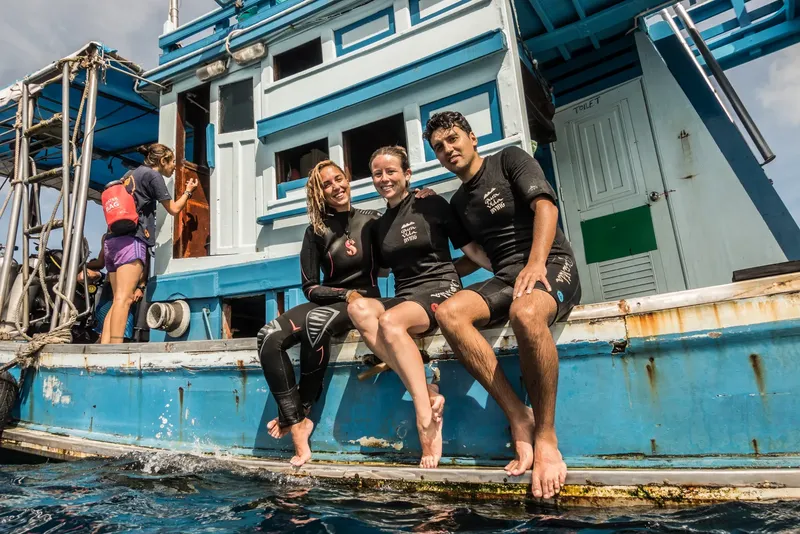 Trois plongeurs souriants assis au bord d'un bateau bleu