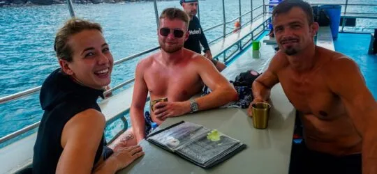 Trois personnes souriantes sur un bateau en mer, ambiance détendue