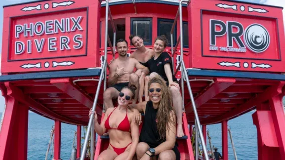 Groupe de personnes souriantes posant sur un bateau de plongée rouge