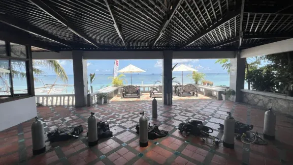 Terrasse ombragée avec bouteilles de plongée et mobilier de jardin face à la mer