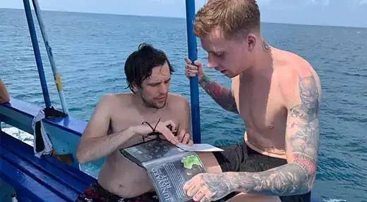 Deux hommes torse nu sur un bateau bleu en mer