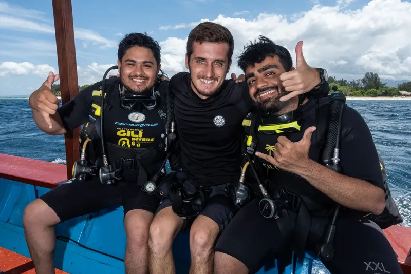 Trois plongeurs souriants sur un bateau, équipés et prêts à plonger