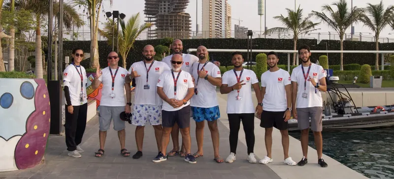Groupe de personnes souriantes posant devant un port de plaisance ensoleillé