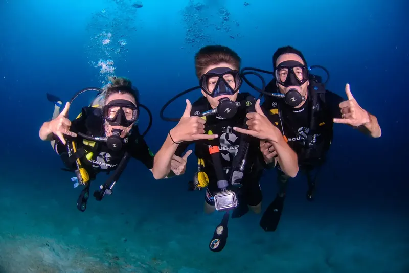 Trois plongeurs souriants font des signes de paix sous l'eau