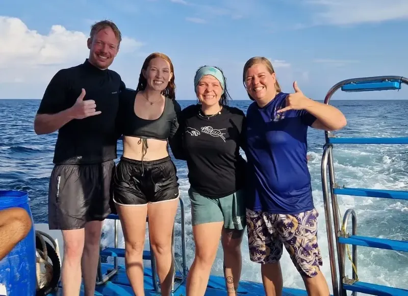 Quatre personnes souriantes sur un bateau en mer, faisant des signes
