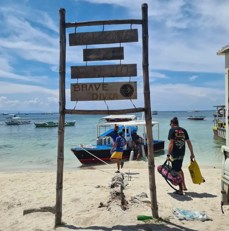 Plage, bateaux de plongée, panneau d'accueil et personnes équipées