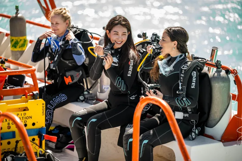 Trois plongeuses souriantes équipées sur un bateau en mer