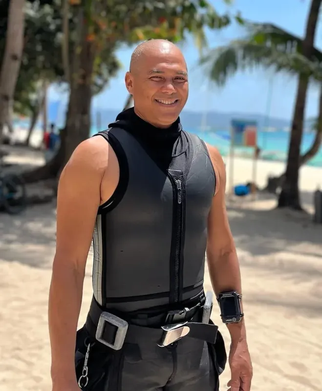 Plongeur souriant sur une plage paradisiaque, équipé d'un gilet et ceinture