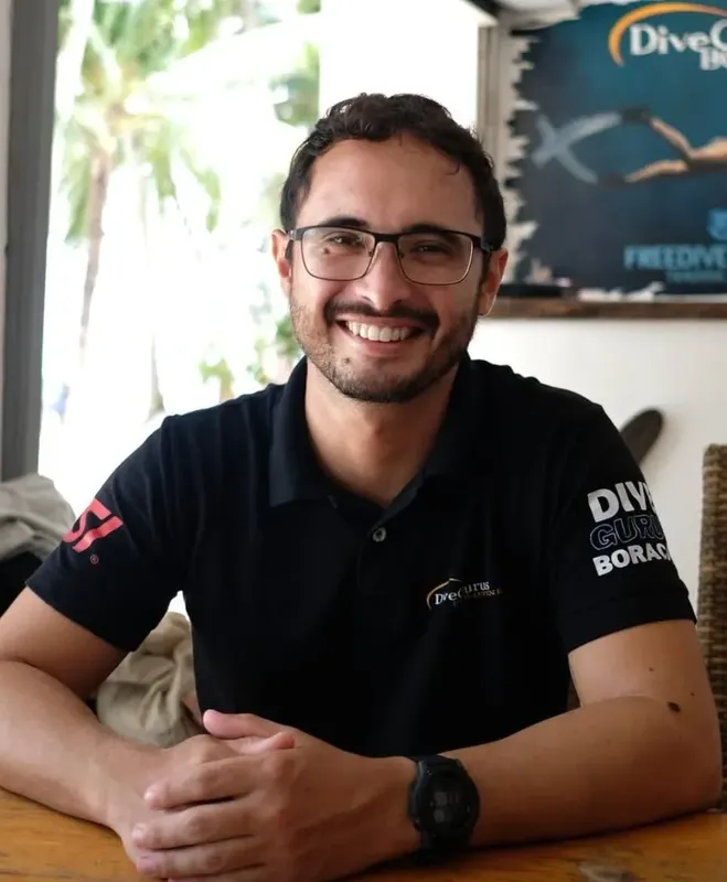 Un homme souriant avec des lunettes, portant un polo de plongée
