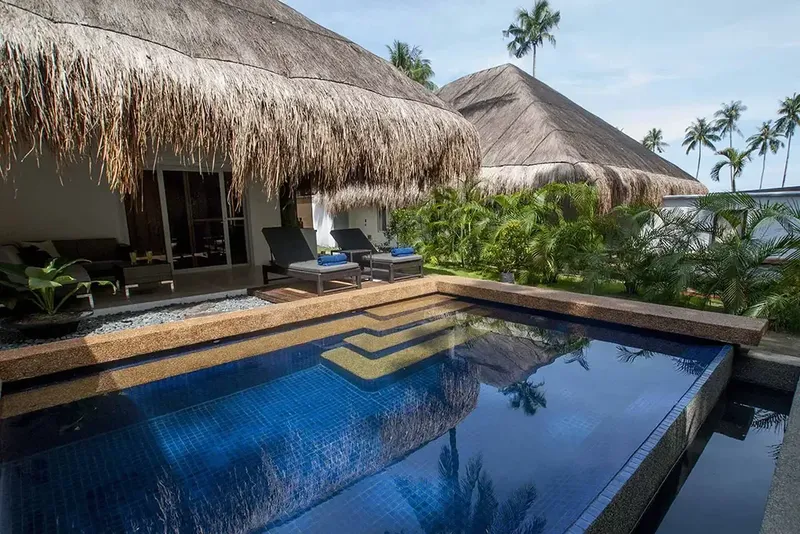 Piscine privée devant des bungalows à toits de chaume tropicaux