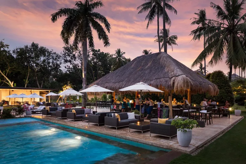 Terrasse avec piscine, bar en chaume et personnes se relaxant