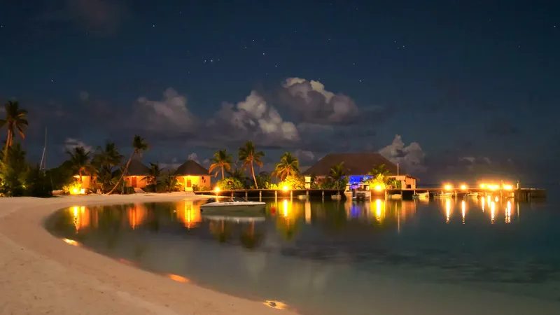 Plage tropicale illuminée la nuit avec un bateau amarré et bâtiments