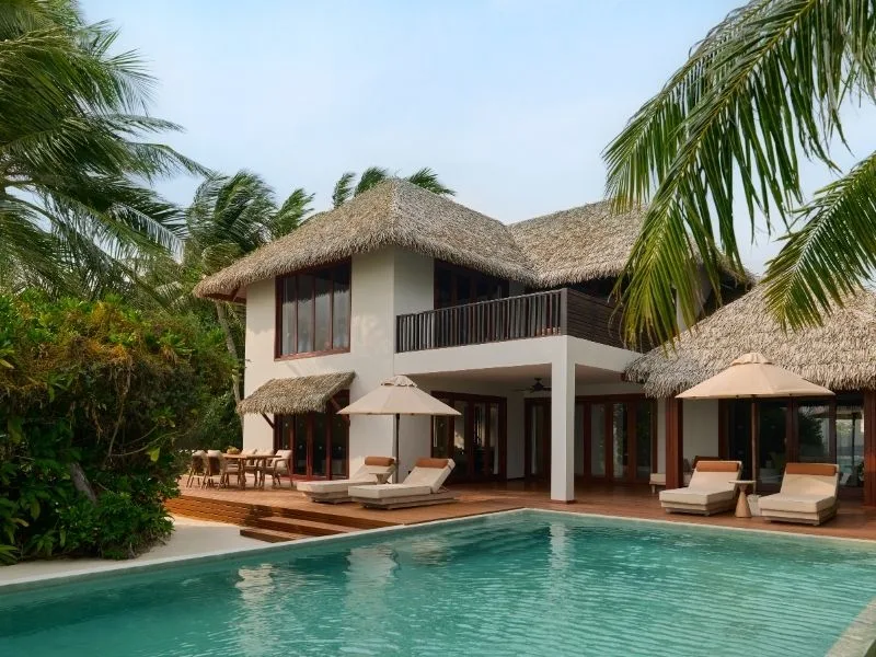 Bâtiment avec toit de chaume, piscine et transats dans un cadre tropical