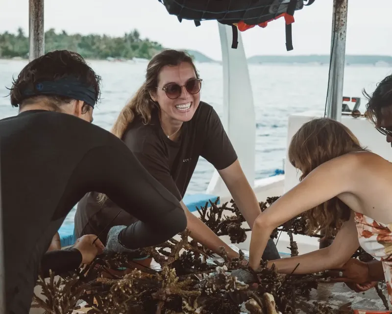 Trois personnes sourient et manipulent des coraux sur un bateau