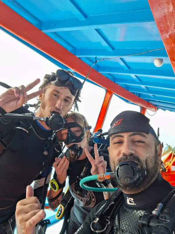 Trois plongeurs souriants font le signe de la victoire avec leurs mains