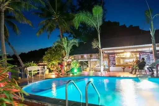Piscine devant un bar avec des palmiers et des personnes assises