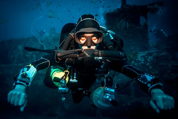 Plongeur en combinaison noire face caméra, exploration sous-marine, épave floue