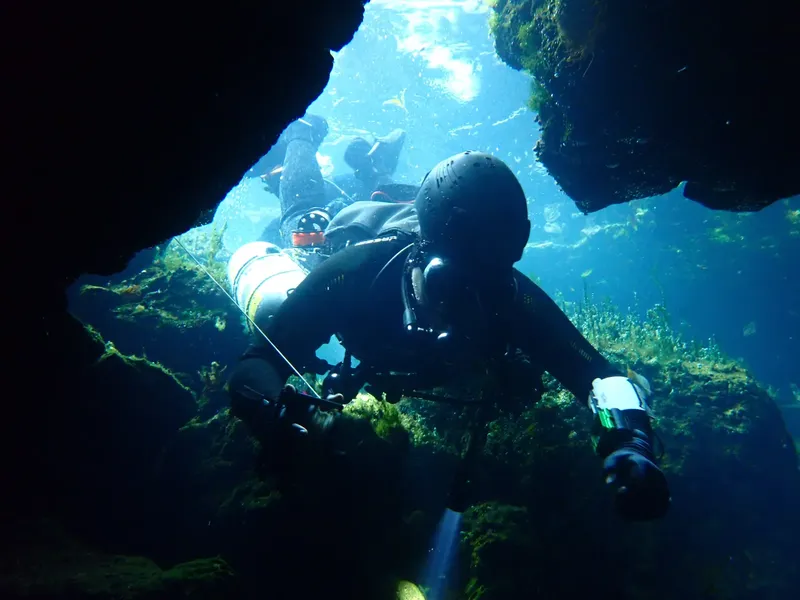 Deux plongeurs explorent une grotte sous-marine, lumière filtrée, ambiance mystérieuse