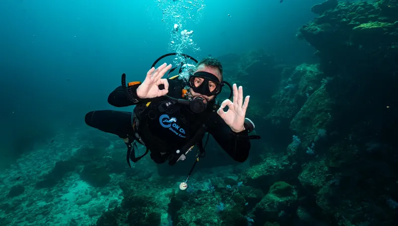 Plongeur souriant avec signe OK, en immersion dans une eau turquoise