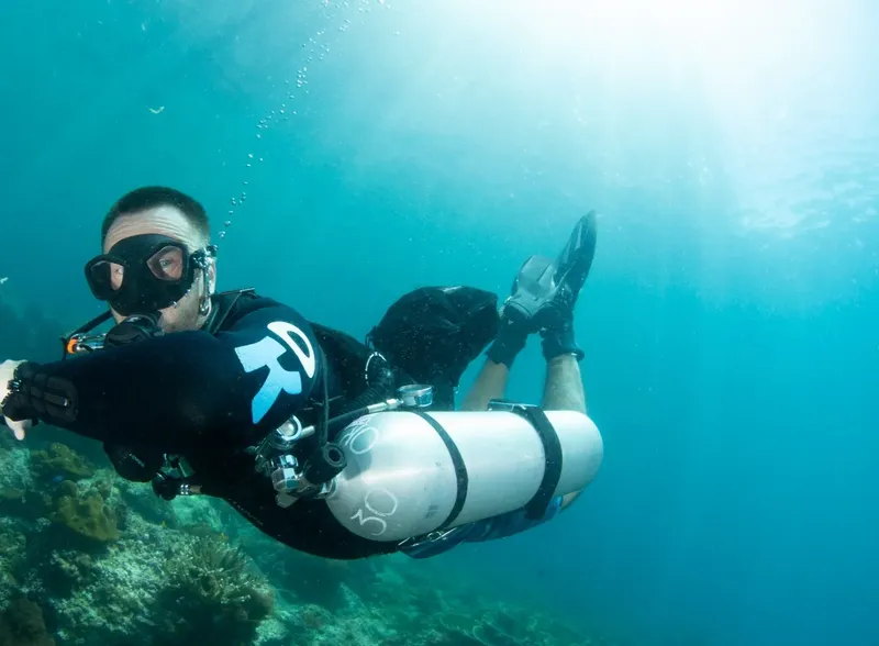 Plongeur en combinaison noire nageant dans une eau turquoise claire