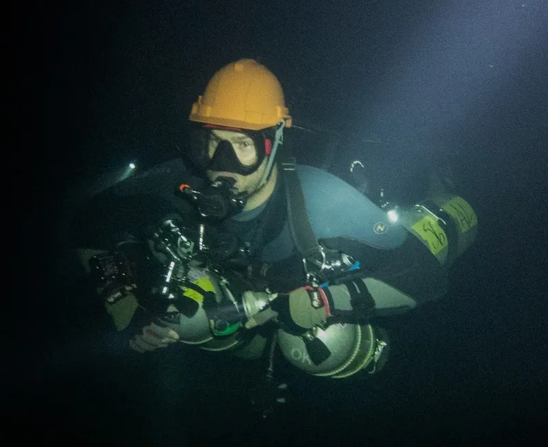 Plongeur équipé d'un casque et d'un détendeur dans l'eau sombre